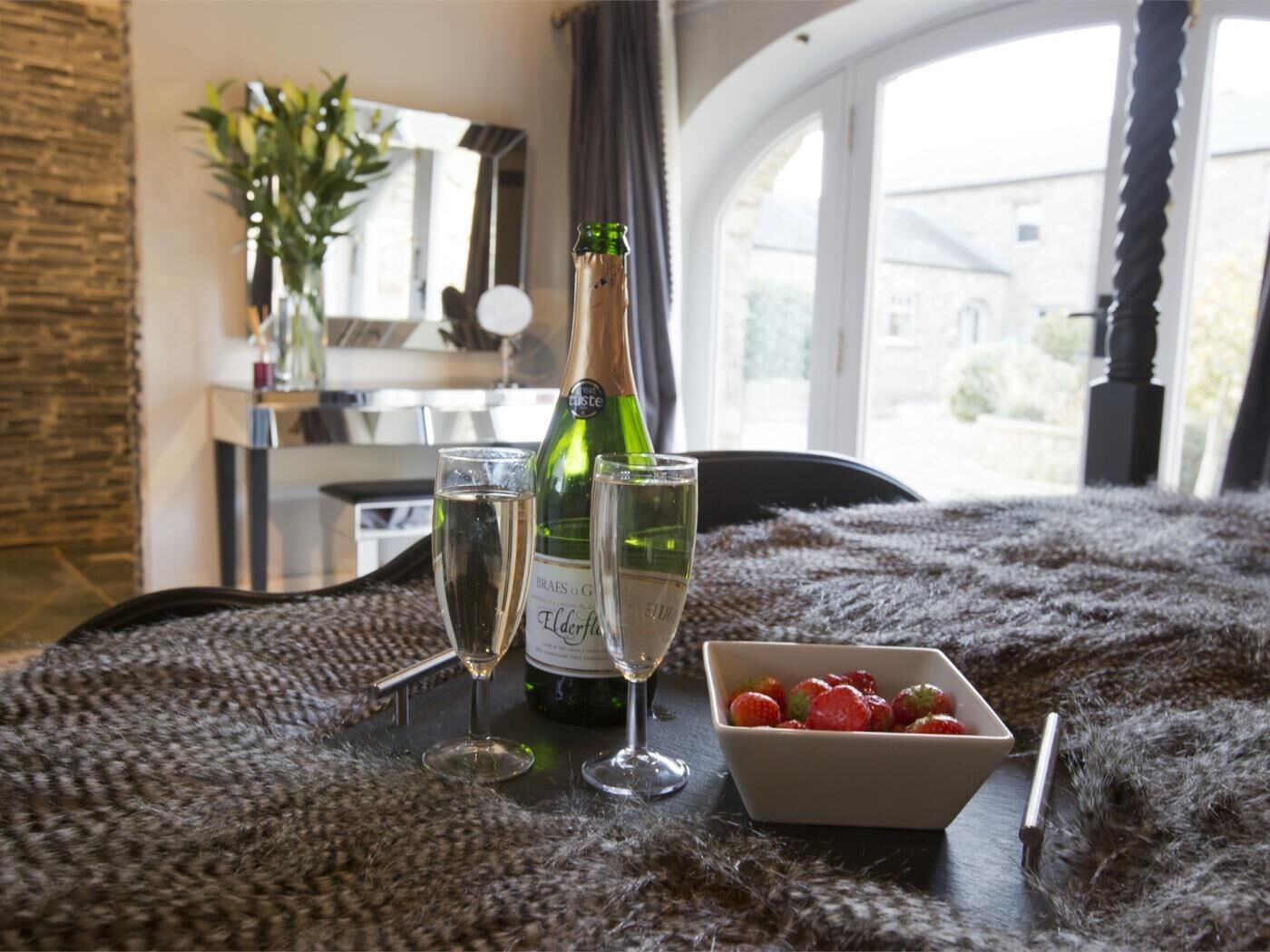 A room with a dining table set for two, a bottle of wine, two glasses, and a bowl of strawberries.