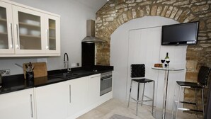 Eine moderne Küche mit weißen Schränken, einer Steinwand, einem Fernseher und zwei Barhocker.