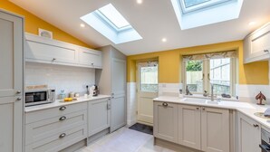 Une cuisine moderne dotée de fenêtres de toit, de meubles blancs et d’un mur d’accent jaune.