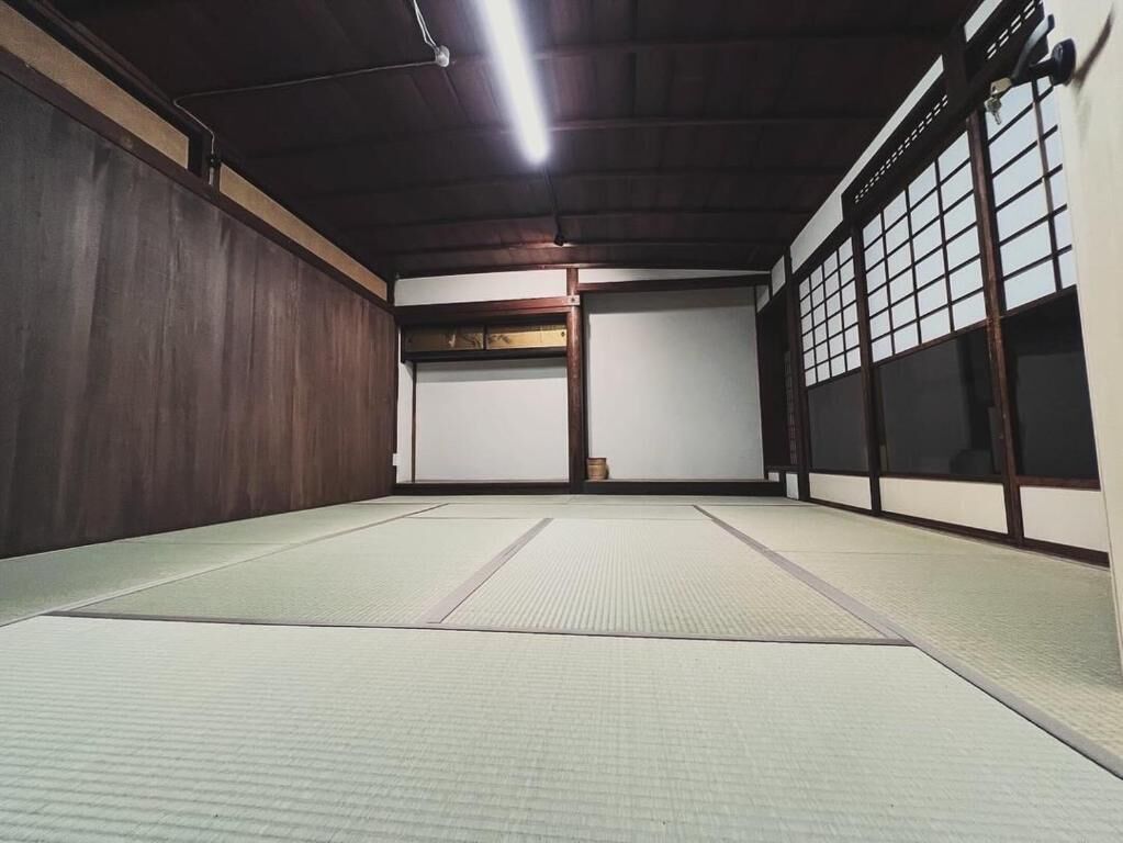Habitación con tatami, techo de madera, puertas correderas y un ventanal grande con divisiones en cuadrícula.