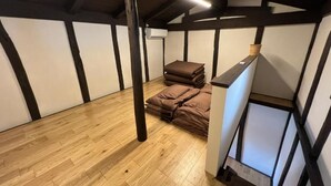 A room with wooden flooring, a loft area with a staircase, and a stack of brown blankets. - HOBOIE Guest House (Tsuruga)