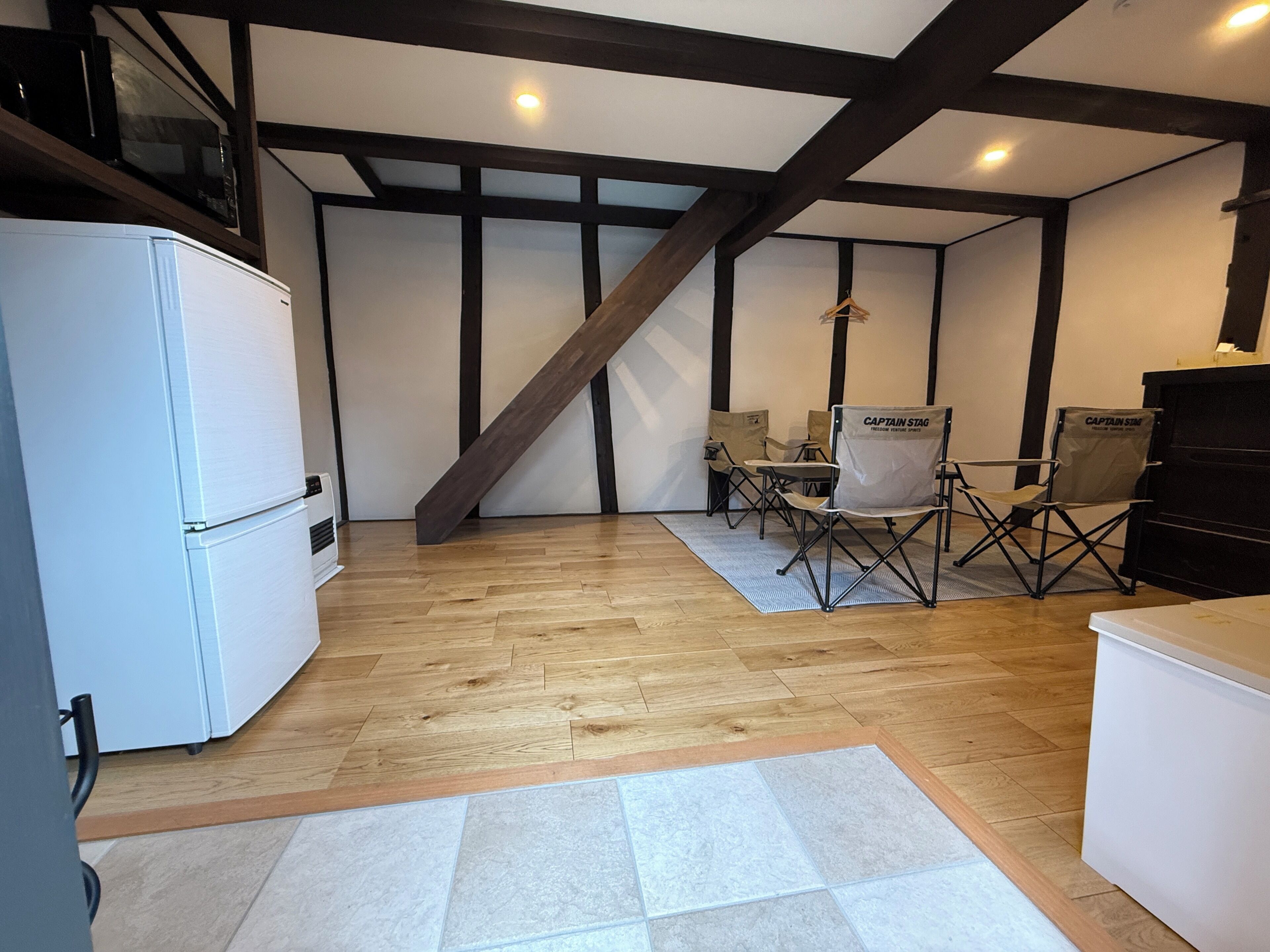 A kitchen with a white refrigerator, wooden flooring, a herringbone ceiling, and a dining area with a table and chairs.