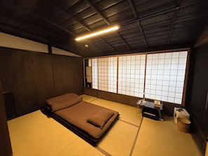 A traditional Japanese room with tatami flooring, a futon bed, a shoji screen, and a ceiling fan.