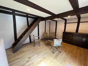 Una habitación con techo inclinado, vigas de madera, una mesa de comedor con sillas y un armario.