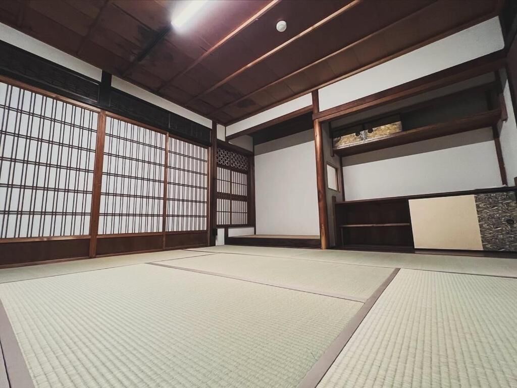 A traditional Japanese room with tatami flooring, sliding doors, and a low wooden ceiling.