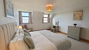 Une chambre à coucher avec un lit, un bureau, une commode et une fenêtre avec des rideaux.