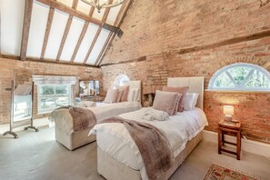 A bedroom with two beds, a large mirror, a window, and a brick wall.