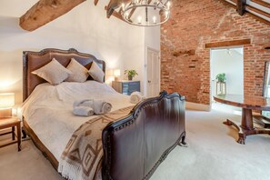 A bedroom with a large bed, a chandelier, a brick wall, and a wooden table. - 2 Bed in Caenby (oc-o35799) (Caenby)
