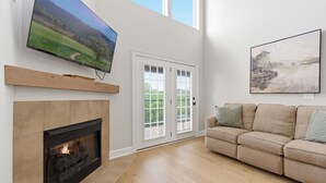 Ein Wohnzimmer mit Kamin, Flachbildfernseher, einer Couch und einer Tür zum Garten.