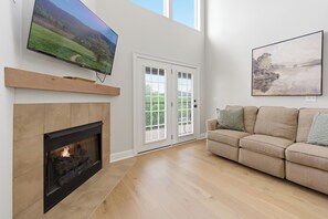 A living room with a fireplace, a flat-screen TV, a sofa, and a door leading outside. - Spacious 3-bedroom condo with River and Mountain Views (Sevierville)