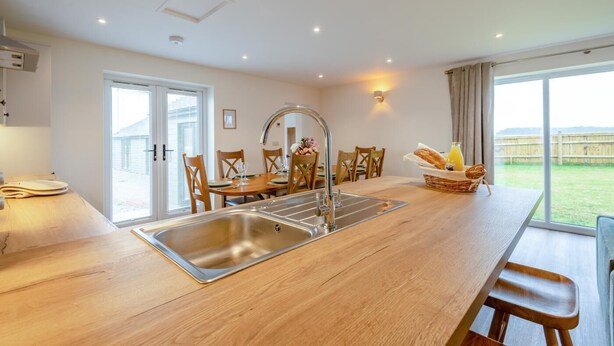 Une cuisine moderne dotée d’un îlot central, d’un coin repas avec des chaises en bois et d’une vue sur l’extérieur.