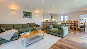 Un salon moderne avec deux canapés verts, une table basse en bois et une cuisine en arrière-plan.