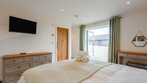 Une chambre à coucher avec un lit, une télévision, une porte en bois, une fenêtre avec des rideaux et une vue sur l’extérieur.