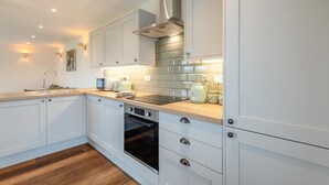 Une cuisine moderne avec des meubles blancs, une hotte en acier inoxydable, un four encastré et un plan de travail en bois.