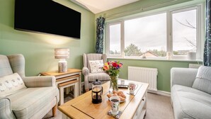 Ein Wohnzimmer mit Sofa, Sessel, Couchtisch und einem an der Wand befestigten Flachbildfernseher.