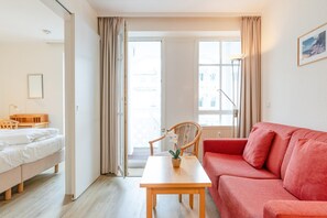 A room with a bed, a red sofa, a wooden table with a plant, and a chair. - Ferienwohnung im Seepark Sellin mit Balkon und Wlan (Sellin)
