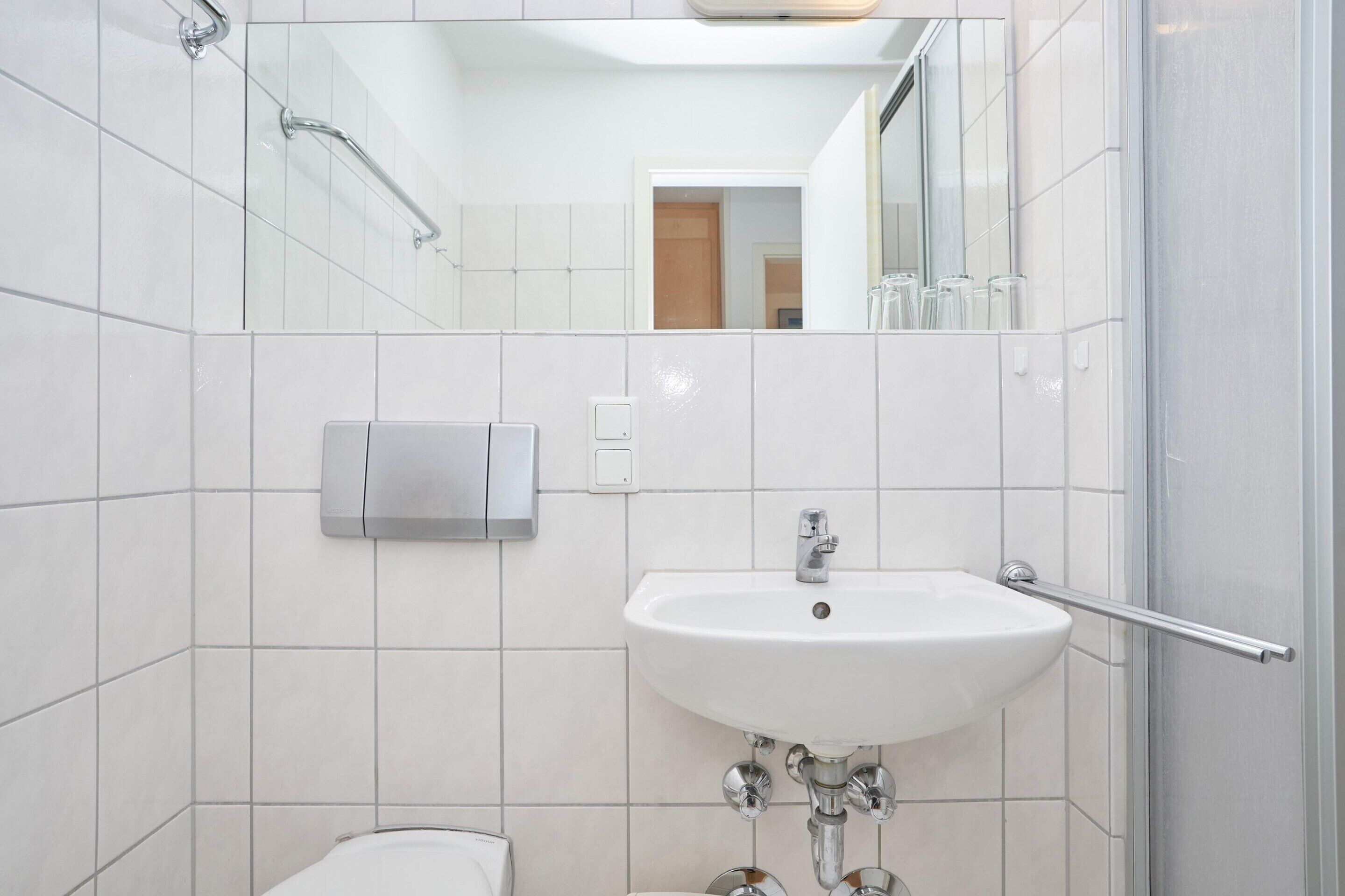 Un baño moderno con un lavamanos blanco, un secador de manos y una cabina de ducha con mampara de vidrio.
