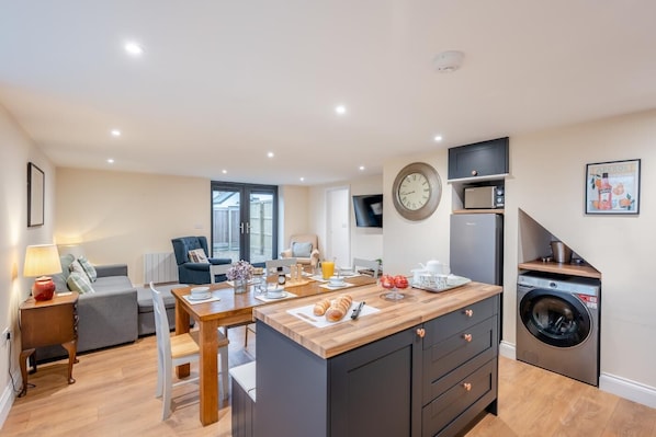 A modern kitchen with a central island, built-in appliances, and a dining area with a sofa and table. - 3 Bed in Feering (oc-hen6) (Feering)