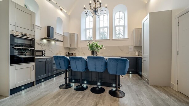 Een moderne keuken met een centraal eiland, barstoelen en een kroonluchter.