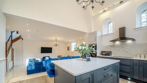 Een ruime woonkamer met een groot eiland, donkere kastjes en een moderne keuken met een marmeren achterwand.