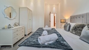 A bedroom with a bed, a bedside table with a lamp, a wardrobe, a mirror, and a dresser. - 6 Bed in High Bonnybridge (oc-b36040) (Bonnybridge)
