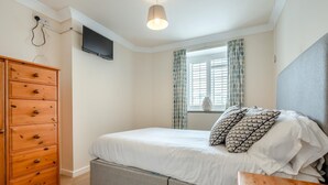 Une chambre à coucher avec un lit, une commode, un téléviseur et une fenêtre avec des rideaux.