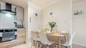 Une cuisine moderne équipée d’une cuisinière, d’un four et d’un grille-pain. On y trouve une table à manger avec des chaises et un vase rempli de fleurs.