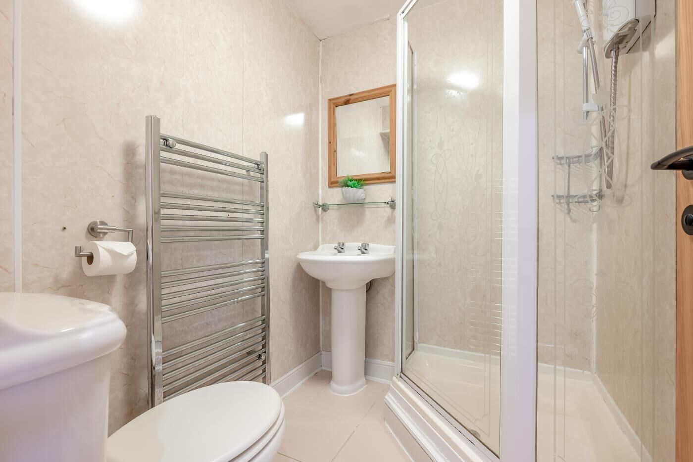 A bathroom with a toilet, a glass-enclosed shower, a sink, and a towel rack.