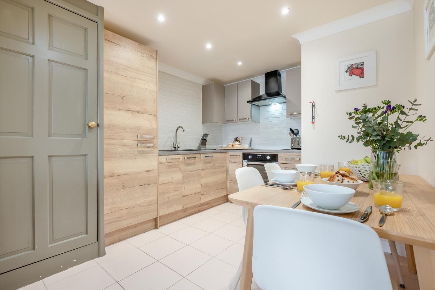 A modern kitchen with wooden cabinets, a dining table with chairs, and a vase with flowers.