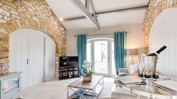 Een moderne woonkamer met stenen muren, een open haard, een televisie en een eethoek met een tafel en stoelen.