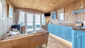 Une pièce chaleureuse avec un plafond en bois, un canapé, une télévision et un coin cuisine doté de meubles bleus.