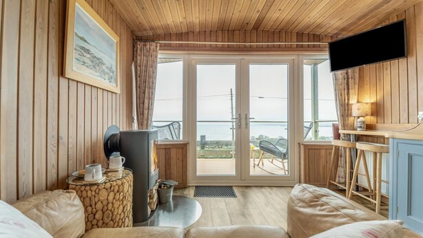 Une pièce chaleureuse avec un plafond en bois, une cheminée, un canapé, une télévision et une vue sur la mer.