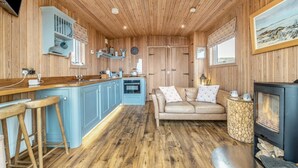 Un intérieur en bois comprenant une cuisine, un coin repas et un salon, avec une cheminée et un pilier en pierre.