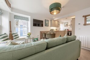 Una sala de estar moderna con un sofá verde, una mesa de comedor con sillas, una zona de cocina y un amplio ventanal con vistas.