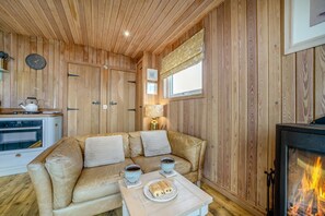 A cozy room with a wooden interior, a sofa, a table with a plate of food and drinks, a fireplace, and a clock on the wall.