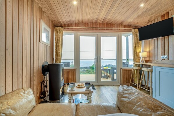 A cozy room with a sofa, a table with drinks, a TV, and a view of the sea.