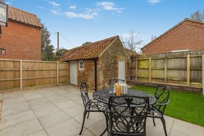 Eine Terrasse mit einem runden Tisch und Stühlen, ein kleines Steinhaus und ein Holzzaun.