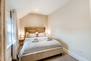 Un dormitorio con una cama grande, lámparas de noche, una ventana con cortinas y un enchufe de pared.