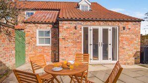 A brick house with a tiled roof, a green door, and a patio with a round wooden table and chairs. - 2 Bed in Haxby (oc-t36047) (Haxby)