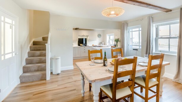A dining area with a wooden table and chairs, a staircase, and a kitchen in the background. - 2 Bed in Haxby (oc-t36047) (Haxby)