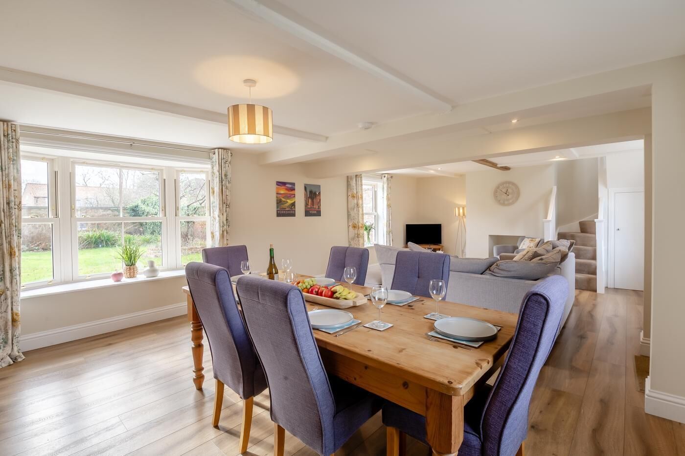 A dining area with a wooden table, chairs, and a dining set. There is a sofa and a television in the background.