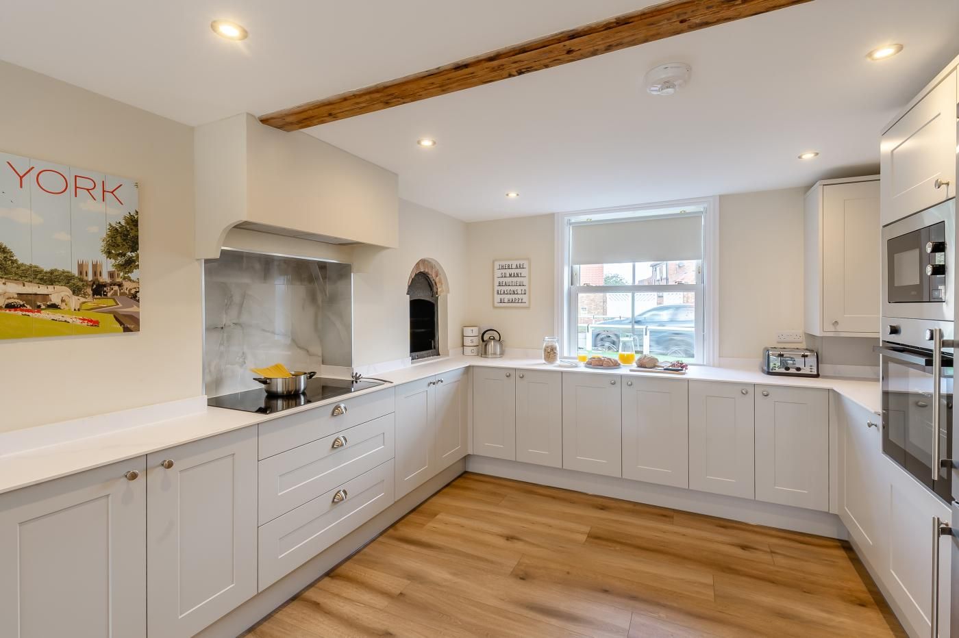 A modern kitchen with white cabinetry, a marble backsplash, and a wooden ceiling beam.