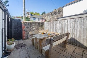 A wooden table and bench in a backyard with a stone wall and a black gate. - 2 Bed in Conwy (oc-t36008) (Conwy)
