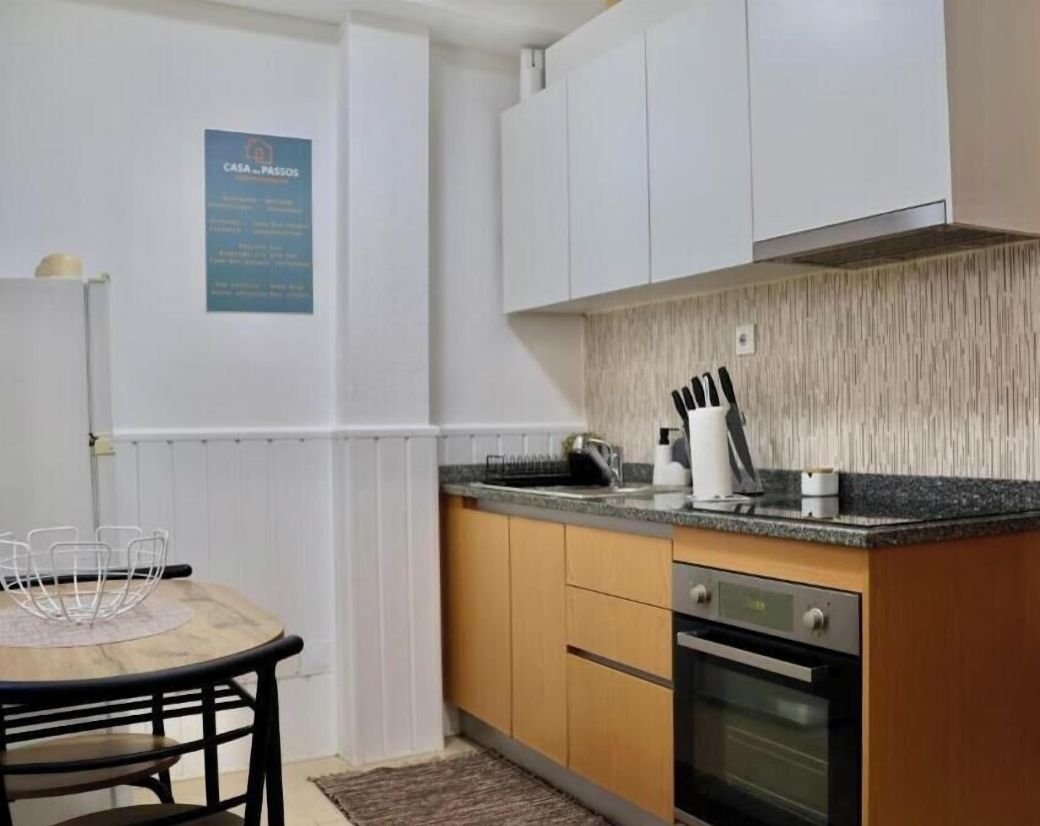 A kitchen with white cabinets, a granite countertop, a built-in oven, and a dining area with a table and chairs.