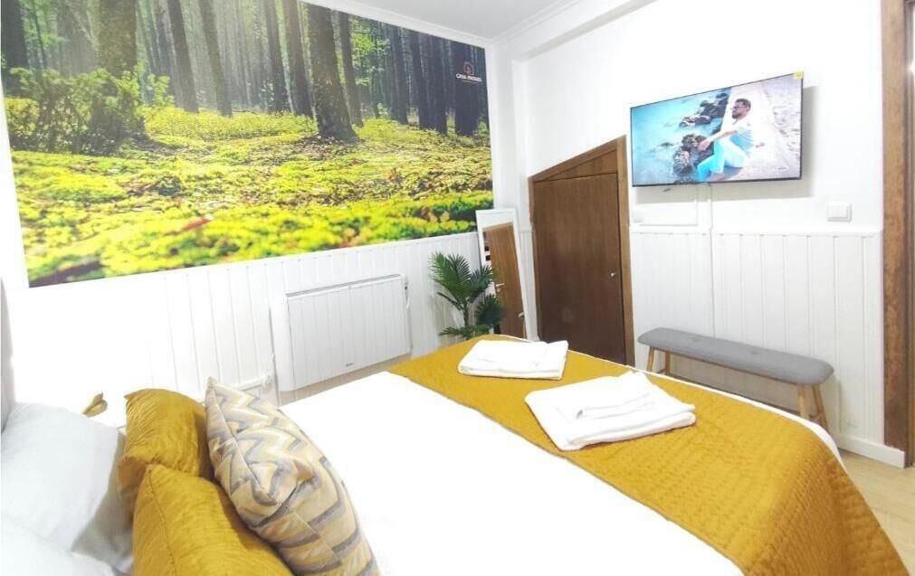A bedroom with a bed, a bench, a TV, and a large forest mural.