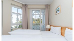 A hotel room with two beds, a window with curtains, a lamp, and a framed picture on the wall. - Auszeit auf Rugen Nahe Ostsee (Sellin)
