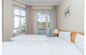 Ein Hotelzimmer mit zwei Betten, einem Fenster mit Vorhängen, einer Lampe und einem gerahmten Bild an der Wand.
