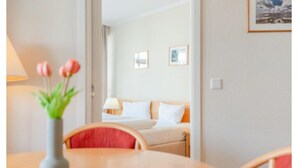 A hotel room with a bed, a bedside table with a lamp, a vase with flowers, and a chair. - Auszeit auf Rugen Nahe Ostsee (Sellin)