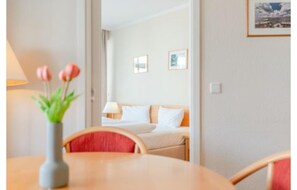 Ein Hotelzimmer mit einem Bett, einem Nachttisch mit Lampe, einer Vase mit Blumen und einem Sessel.
