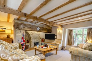 Ein gemütliches Wohnzimmer mit Kamin aus Stein, Holzbalken, einem Fernseher und bequemen Sitzgelegenheiten.